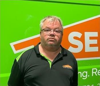 Male employee with gray hair in front of wall