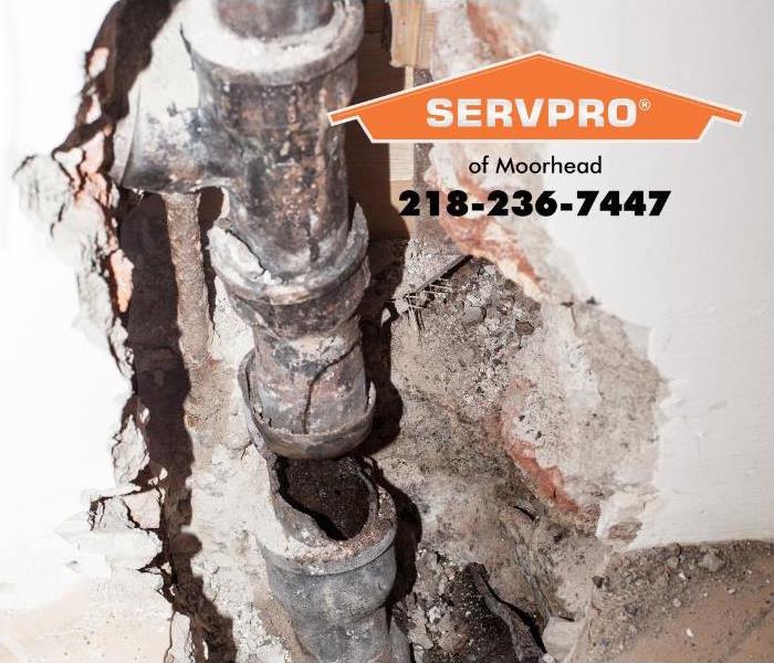 A wall has been opened, exposing a broken sewage pipe and corroded plumbing pipes.